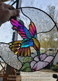 a hand holding up a stained glass window with a hummingbird on it's side