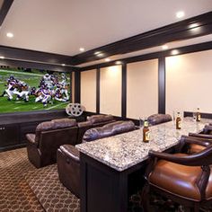 a home theater with leather chairs and a large television screen on the wall behind it