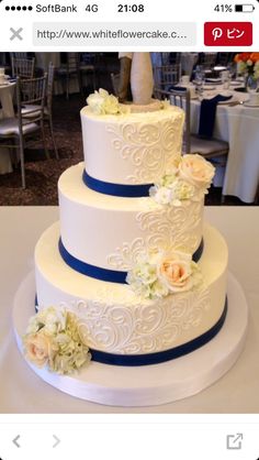 a three tiered wedding cake with blue ribbon and flowers on the top, sitting on a table