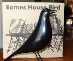 a black bird statue sitting on top of a wooden table next to a sign that says eames house bird