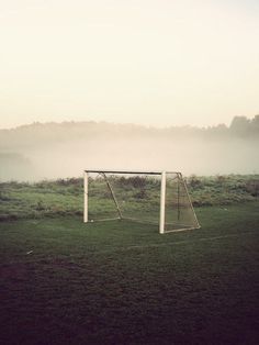 a soccer goal sitting on top of a field next to a lush green field covered in fog