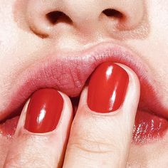 a close up of a woman's hand with red nail polish on her lips