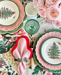 a table topped with plates covered in pink flowers and green trimmings next to white dishes