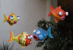 three colorful fish hanging from strings in front of a building with plants and potted plant