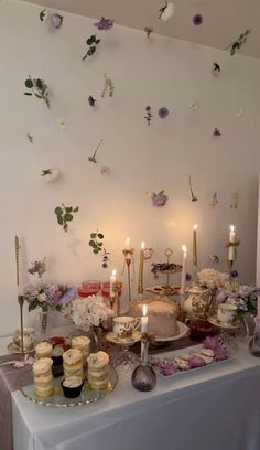 a table topped with lots of cakes and cupcakes on top of a white table cloth