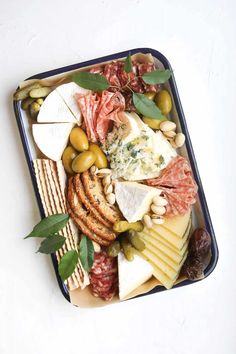 an assortment of cheeses, meats and olives on a platter with leaves