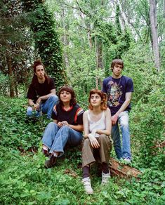 four people are sitting in the woods and posing for a photo with trees behind them