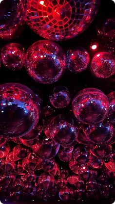 many shiny glass balls are stacked on top of each other in the dark, with red lights shining through them