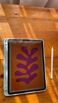 a wooden table topped with a tablet computer next to a white pen and paper on top of it