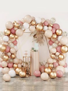 a large balloon arch with gold, pink and white balloons on it's sides