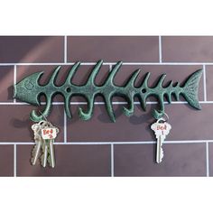 three fish skeleton keys hang on a brick wall next to two key hooks with the same shape