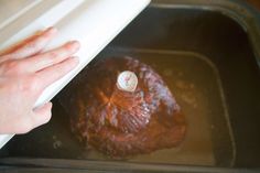 a person is placing something on top of a roasting pan with meat in it