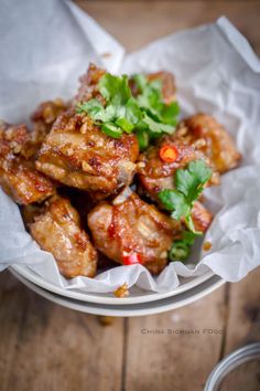 chicken wings with cilantro and green garnish in a white bowl on a wooden table