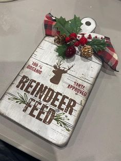 a wooden sign that says reindeer feed with pine cones and berries on it, sitting on top of a table