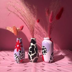 three vases with flowers in them sitting on a pink tableclothed surface against a pink wall