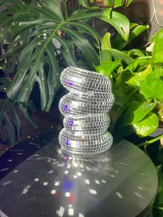 a stack of disco balls sitting on top of a metal table next to green plants