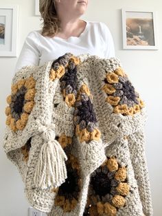 a woman is holding up a crocheted blanket