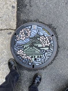 a man's feet standing on the sidewalk next to a sewer cover with flowers painted on it