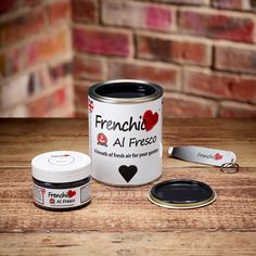 a can of french paint next to a keychain on a wooden table with a brick wall in the background