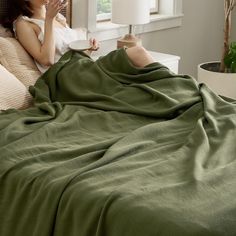 a woman laying in bed covered with a green blanket and covering her face next to a window