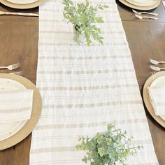 the table is set with plates, silverware and green plants in vases on it