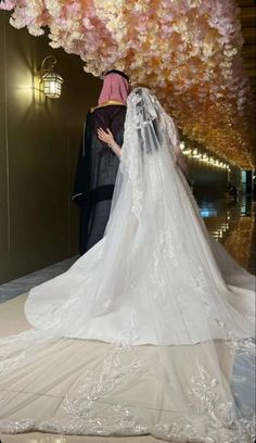 the bride and groom are standing under a flower covered tree in their wedding dress, which is adorned with pink flowers