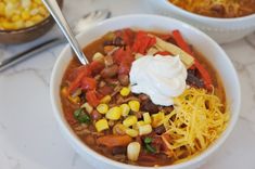 two bowls of chili and corn with sour cream on top, one bowl is full