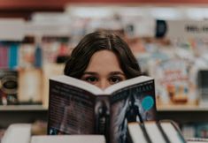 a woman reading a book in front of bookshelves at a bookstore or library