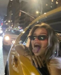 a woman sticking her tongue out in the back of a yellow car on a city street