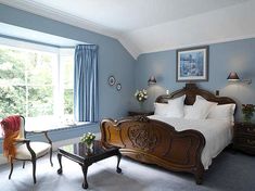 a bed room with a neatly made bed next to two chairs and a table in front of a window