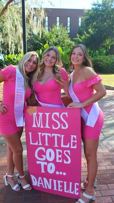 three women in pink dresses are holding a sign that says miss little goes to danielle