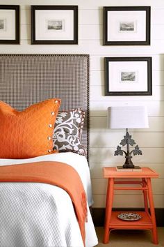 an orange and white bedroom with pictures on the wall above the bed, side table