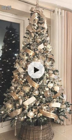 a christmas tree decorated with gold ribbon and ornaments in a living room area, next to a window