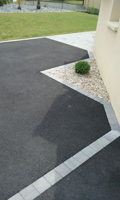 an empty parking lot in front of a building with grass and bushes on the side