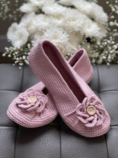 pink crocheted baby shoes sitting on top of a black leather seat next to white flowers