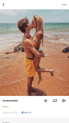 a man and woman kissing on the beach while holding each other in front of them