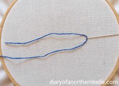 a close up of a blue thread on a white cloth with a wooden hoop in the background