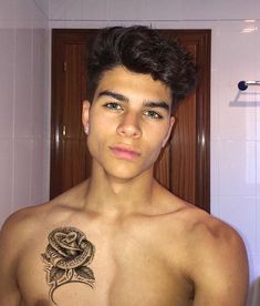 a young man with a snake tattoo on his chest in the bathroom, looking at the camera