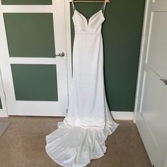 a white wedding dress hanging on a hanger in front of a green painted wall