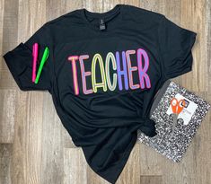 a t - shirt with the word teacher on it next to a pair of scissors