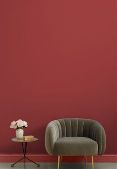 a chair next to a table with a vase on it and a red wall in the background