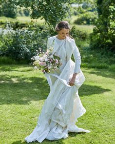 a woman in a wedding dress walking through the grass