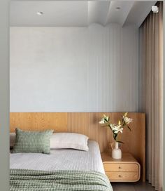 a bed with green and white pillows in a bedroom next to a nightstand filled with flowers