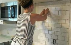 a woman is painting the backs of a kitchen wall with white tile and red paint