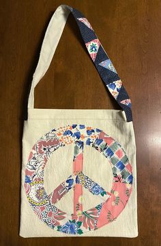 a peace sign on a tote bag hanging from a wooden table with a blue and white ribbon