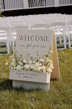 a welcome sign sitting in the grass next to rows of chairs with flowers on them