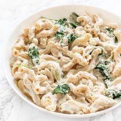 a white bowl filled with pasta and spinach on top of a marble countertop