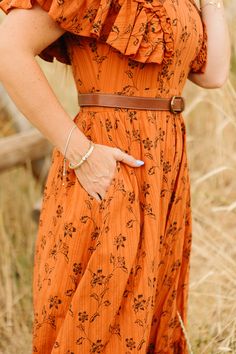 Add a pop of fun to your wardrobe with our Shae Dress in Burnt Orange. This playful women's dress features a unique orange and brown floral print, a high neckline with feminine ruffle detailing, and short flutter sleeves. With its ankle length skirt, pockets, and hidden back zipper, this fully lined 100% cotton dress is both stylish and functional. Brown Ruffled Maxi Dress, Orange Flutter Sleeve Dress For Spring, Brown Summer Dresses With Flutter Sleeves, Casual Orange Maxi Dress With Ruffles, Casual Orange Ruffled Maxi Dress, Brown Ruffled Maxi Dress For Spring, Brown Ruffle Hem Midi Dress For Spring, Flowy Brown Maxi Dress With Ruffles, Orange Maxi Dress With Ruffles And Short Sleeves