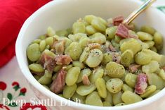 a white bowl filled with green beans and ham on top of a red table cloth