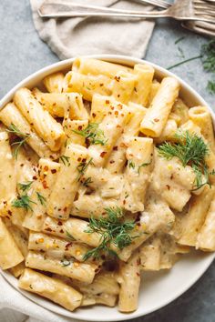 a white bowl filled with pasta covered in sauce and garnished with fresh herbs